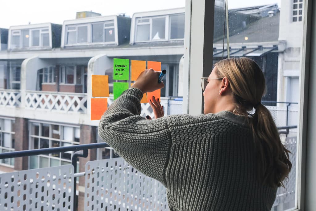 Une personne est en train d’écrire sur un post-it collé à une fenêtre. Cette femme en toute autonomie, prépare son coaching et écris ses idées.